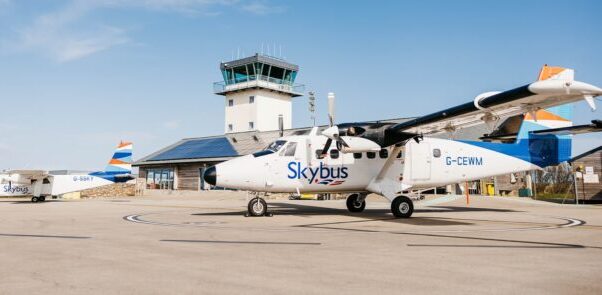 A white Skybus aircraft on the tarmac at an airport. Blue sky in the background.
