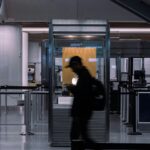A couple silhouettes of people can be seen walking through and past border security at an airport. It is a shutter-speed style photo, stylistically blurred.