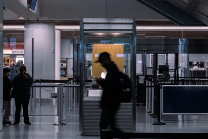 A couple silhouettes of people can be seen walking through and past border security at an airport. It is a shutter-speed style photo, stylistically blurred.