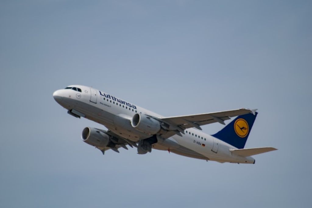 A Lufthansa Airbus A319 aircraft flying midair with a deep blue sky background