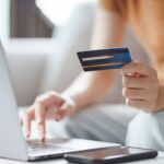 Woman holding credit card while using laptop to book online.