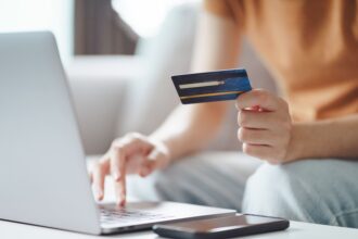 Woman holding credit card while using laptop to book online.