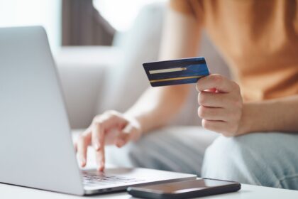 Woman holding credit card while using laptop to book online.