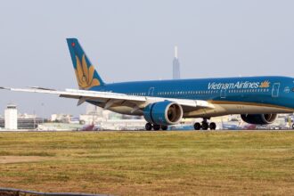 Vietnam Airlines Airbus A350 taxiing on the runway with airport buildings in the background.