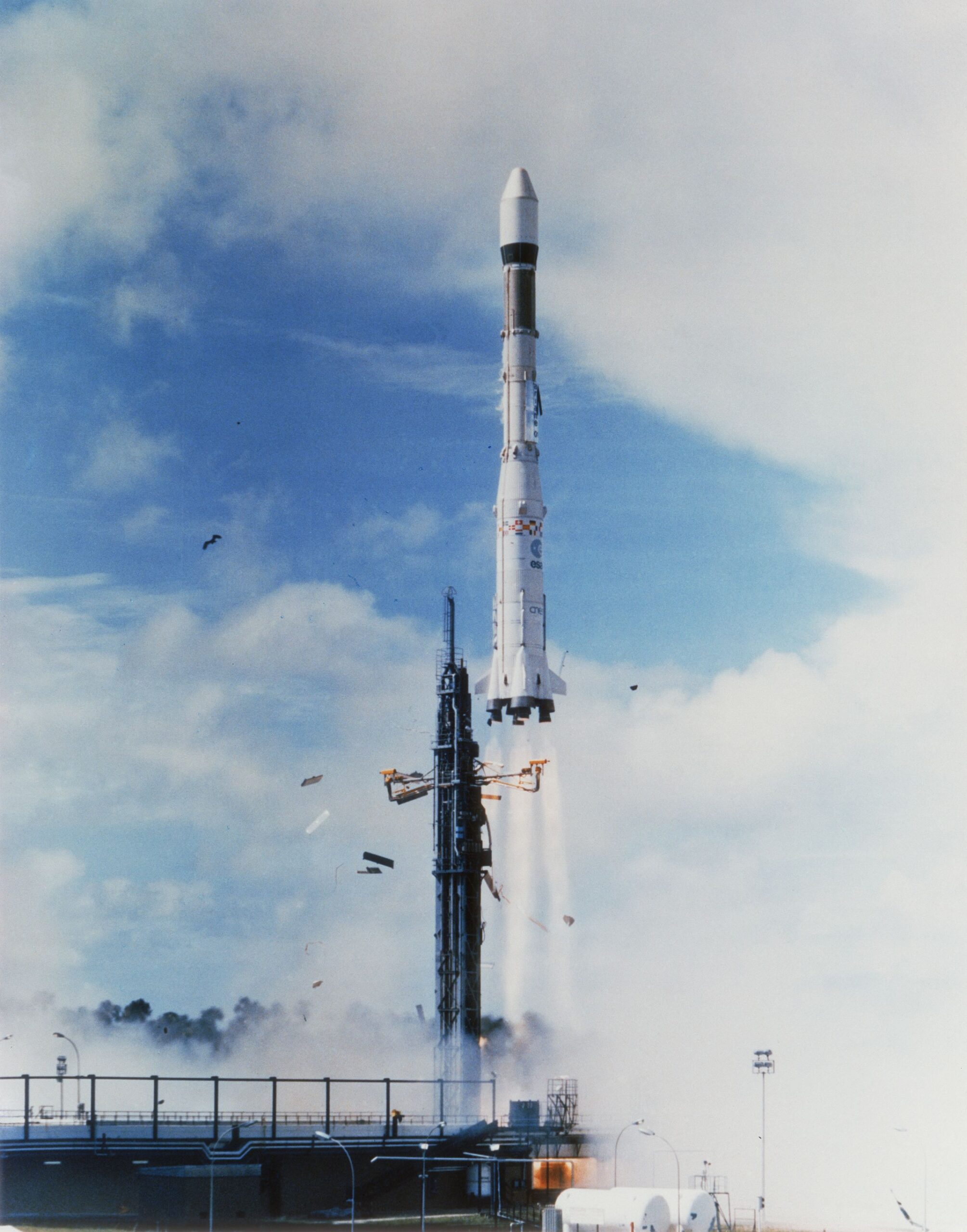 An Ariane 1 launch – a white launch vehicle with a conical cargo fairing on its nose lifts off from a launchpad at Kourou, French Guiana. This spacecraft is similar to that involved in the 1996 collision.