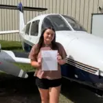 Emily Shelton standing in front of two aircrafts holding a piece of paper.