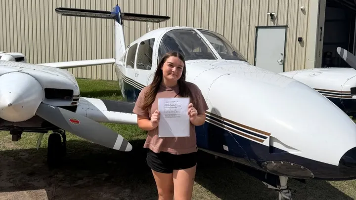 Emily Shelton standing in front of two aircrafts holding a piece of paper.