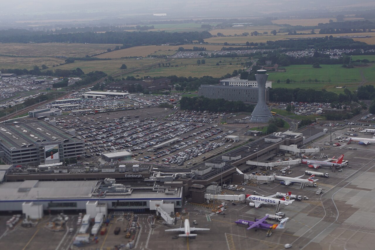 An aerial view of Edinburgh Airport. The weather is grey and it appears misty. There are aircraft dotted around the runway with the control tower standing further off in the distance. 