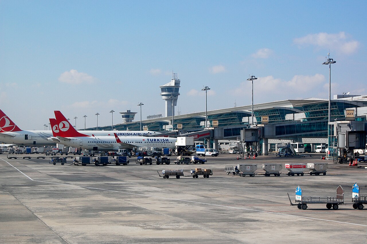 Istanbul Atatürk Airport with Turkish Airline planes on the tarmac, on standby and ready to be boarded. The sky is clear with a few clouds. The airport appears calm and there are no people about.