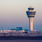 The main control tower of Munich Airport positioned in the distance. The sun is setting causing an ombre of light orange to purple skylight.