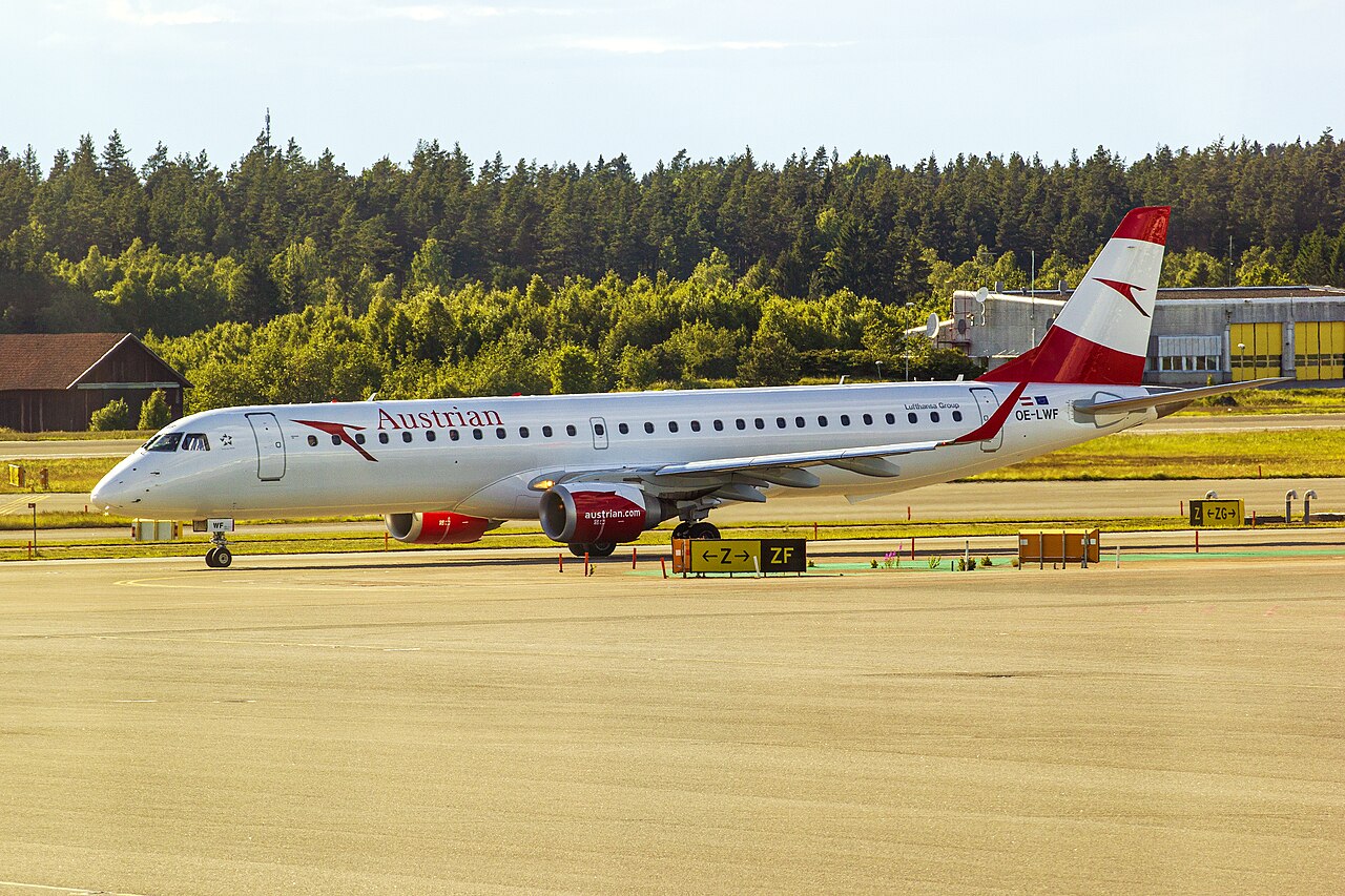 Austrian Airlines Embraer 195 on the runway. Trees can be seen in the background.
