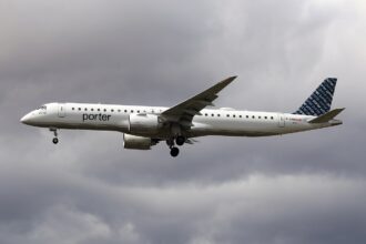 A Porter Airlines Embraer 195-E2 flying under a very cloudy and grey sky. The aircraft's livery is almost entirely white with a dark blue tail.