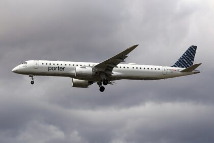A Porter Airlines Embraer 195-E2 flying under a very cloudy and grey sky. The aircraft's livery is almost entirely white with a dark blue tail.