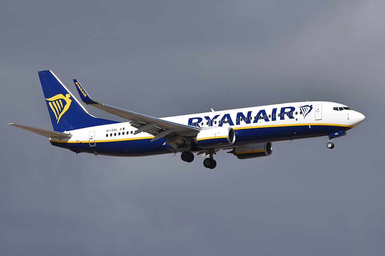 A Ryanair Boeing 737-800 in flight and getting ready to land. The weather is cloudy which makes the colours of the aircraft pop. Ryanair's colours feature blue, white and yellow and can be seen on the aircraft brightly against the moody environment.