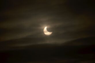 Image shows a dark sky with clouds and white sun and moon shape from 2011 solar eclipse