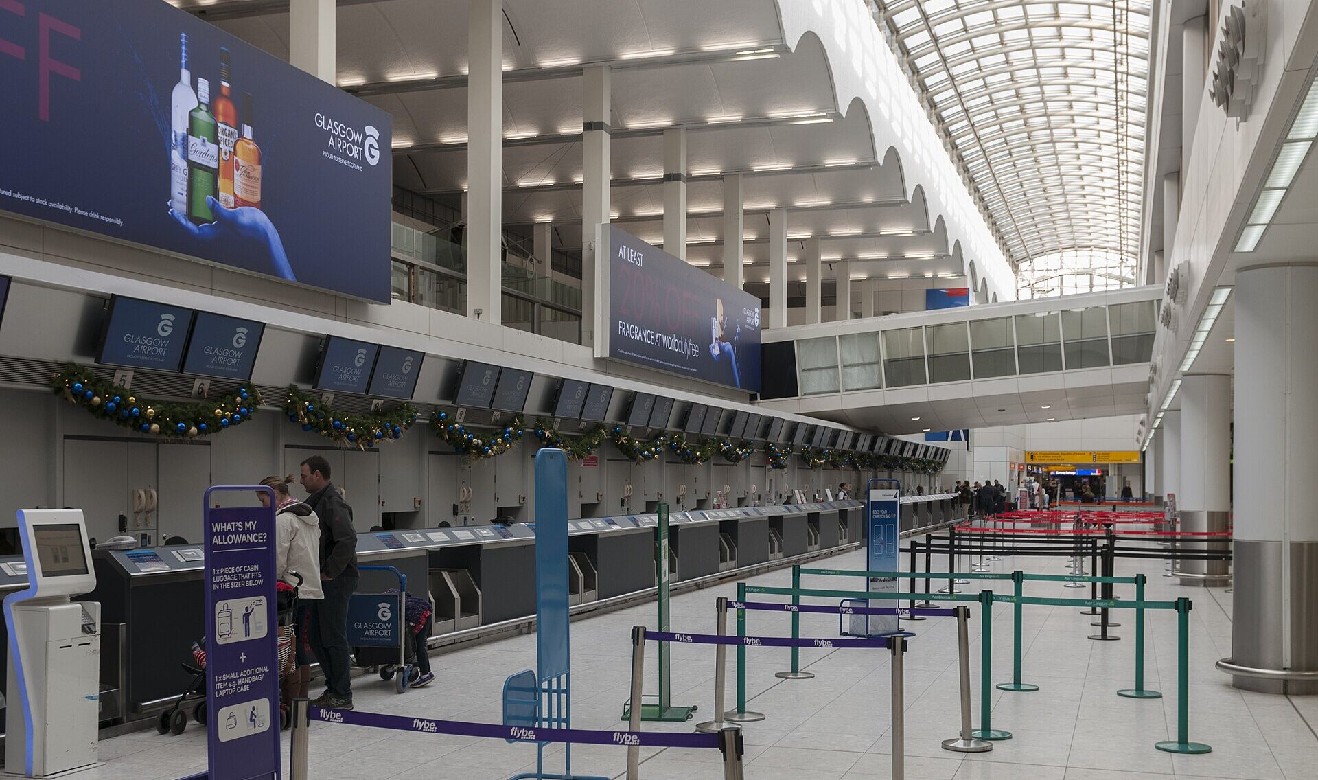 Interior of Glasgow International Airport, wide area with light coming in from the ceiling. Two people at the desk checking their luggage.