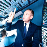 A man dressed in a suit is in the cockpit pointing upwards