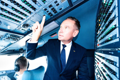 A man dressed in a suit is in the cockpit pointing upwards