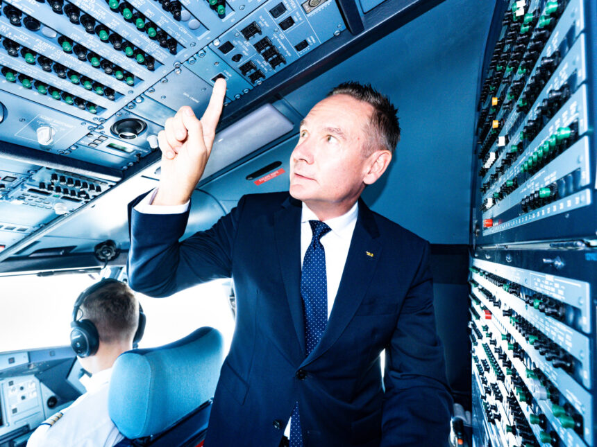 A man dressed in a suit is in the cockpit pointing upwards