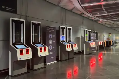 A line of EES kiosks with a large sign that instructs passengers of the registration process.