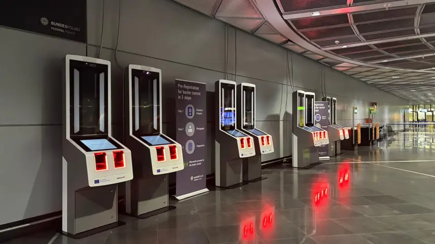 A line of EES kiosks with a large sign that instructs passengers of the registration process.