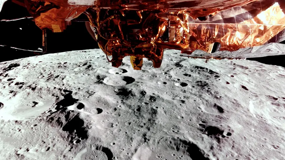 Many craters and mountains on the surface of The Moon seen by Firefly’s Blue Ghost spacecraft, a box covered in gold foil orbiting above, in 2025.