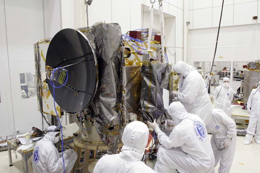 Scientists in “John Hopkins University” boiler suits and masks building a satellite, consisting of a large radio dish and many boxes wrapped in protective material, in one of RAL Space’s cleanrooms.
