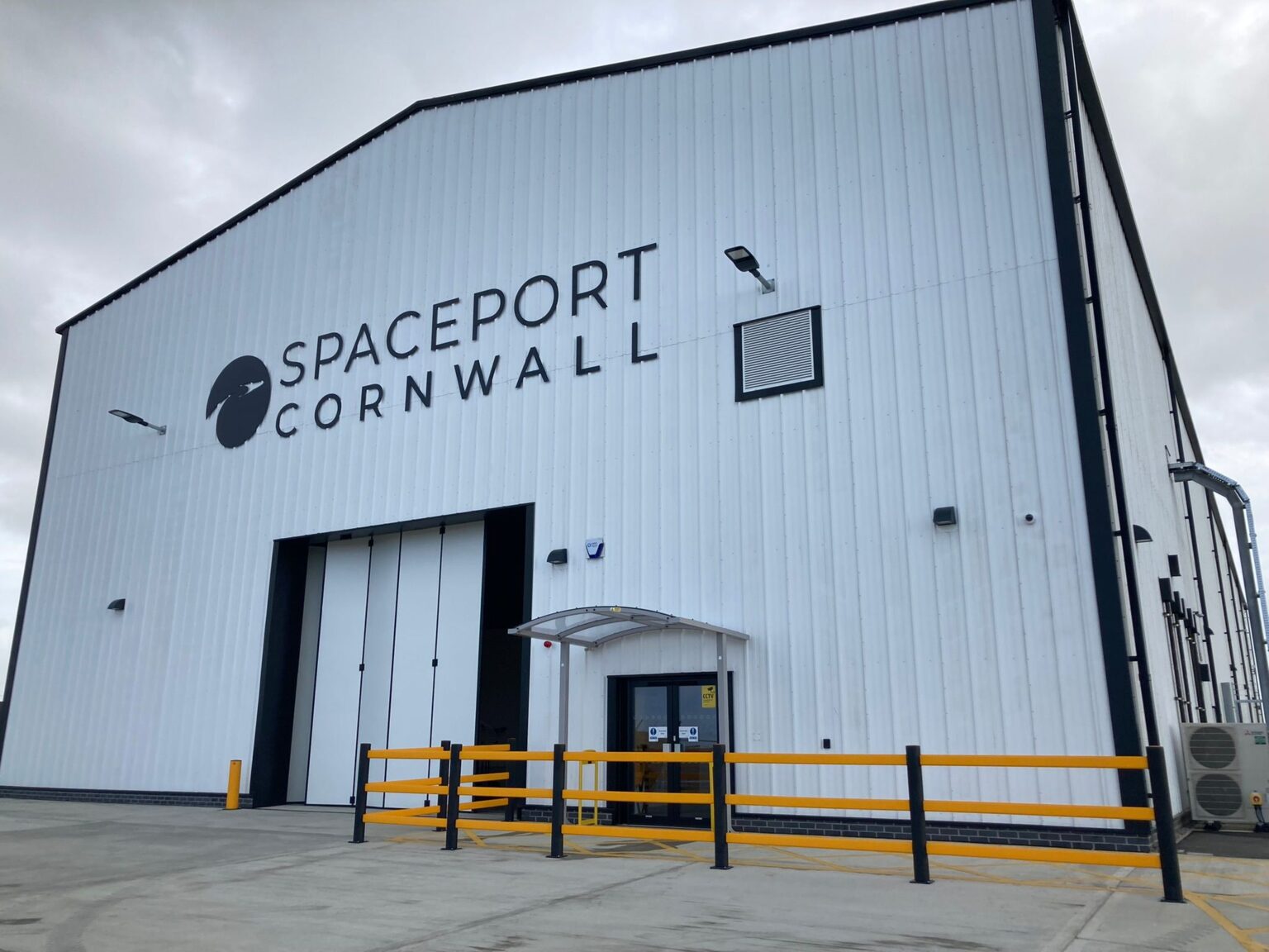 The facility at Spaceport Cornwall - a white hangar with sliding doors and a large "Spaceport Cornwall" logo with railings outside - where Virgin Orbit's LauncherOne mission was prepared.