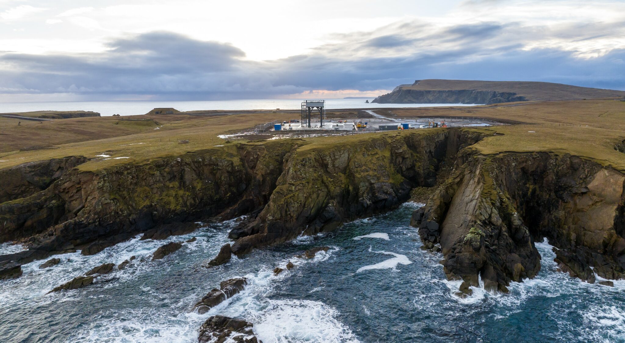 SaxaVord spaceport, a raised concrete and metal launchpad surrounded by buildings near a cliff edge on Shetland.