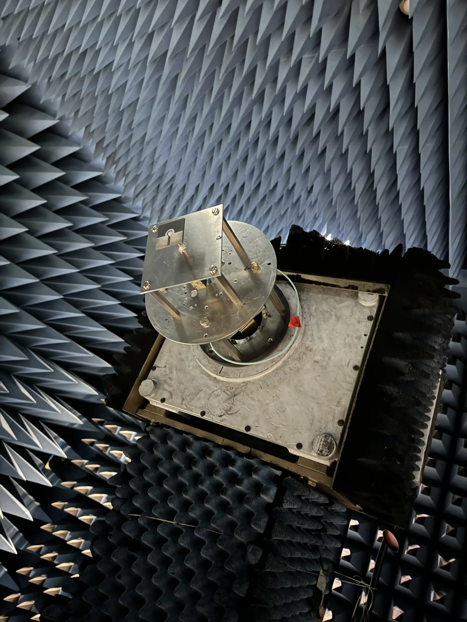 A square, metal 3D-printed antenna, designed by NASA as a low-cost communications device, mounted on a frame and being tested inside an electromagnetic echo chamber with pyramidal foam shapes on the walls for insulation. 3D printing is at the forefront of aerospace design.