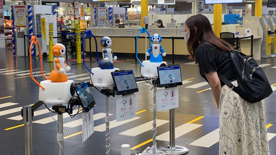 A lady stood in the airport with three robots to help assist in front of her.