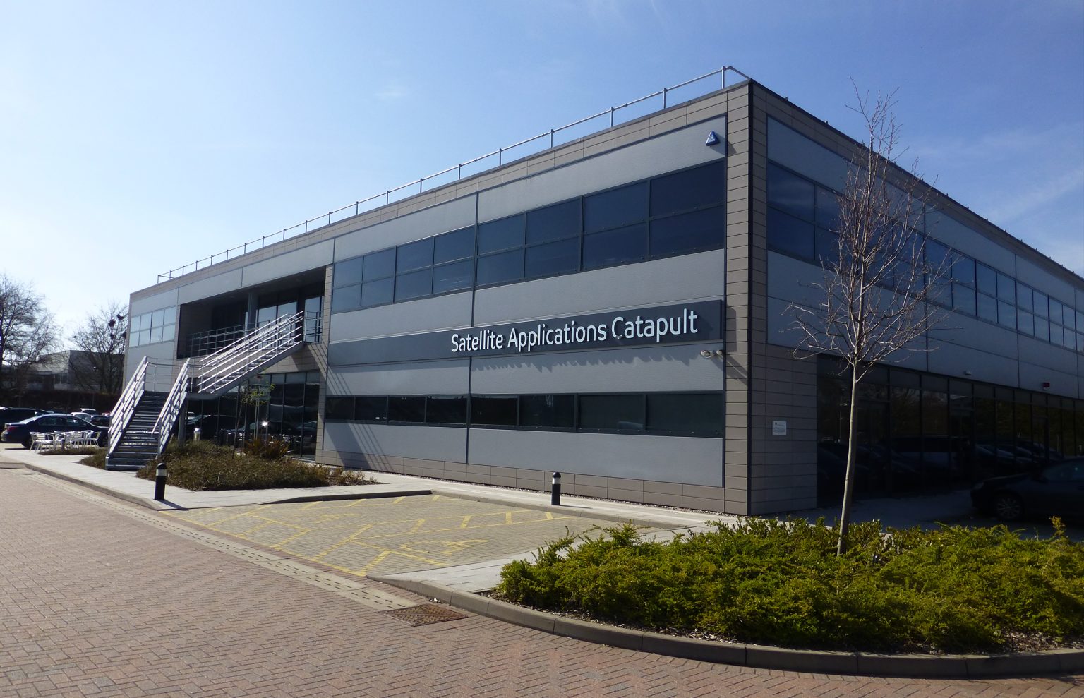 The Satellite Applications Catapult building – a large, grey, cuboidal building with a staircase on the front – in Harwell, Oxfordshire.