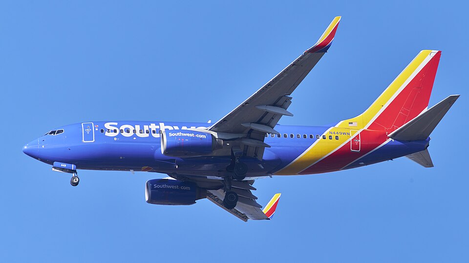 A Southwest Airlines Boeing 737-700 (registration N849WN) on final approach with landing gear extended, featuring the airline's distinctive blue livery with red, yellow, and orange tail stripes, and "Southwest" branding in white along the fuselage, set against a clear blue sky.