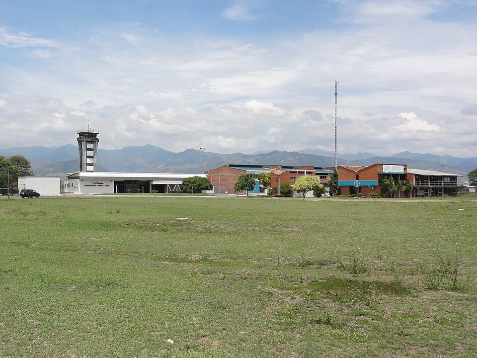 Image shows Santa Ana Airport in Cartago during the day with grass in the foreground, buildings in the background