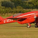 Image shows a grounded red De Havilland DH88 Comet ‘G-ACSS’ aircraft during the day
