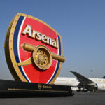 Photograph depicting 3D Arsenal logo positioned in front of an Emirates aircraft on the runway.