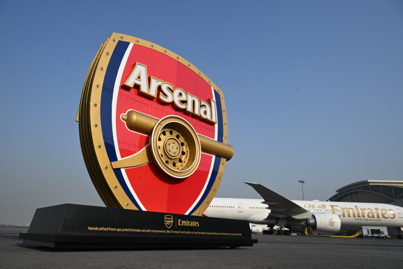 Photograph depicting 3D Arsenal logo positioned in front of an Emirates aircraft on the runway.