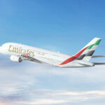 An Emirates Airbus A380 aircraft featuring the flag colors of the UAE on its tail and photographed on its left-hand side