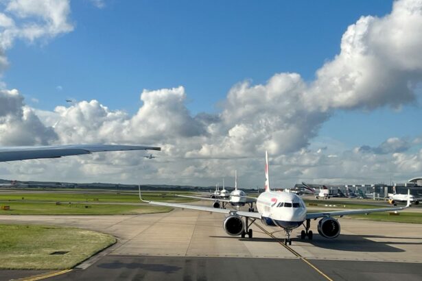 Planes queuing at a Heathrow Airport terminal, with one jet facing the camera. There is Grass on the sides and a blue sky at the backdrop