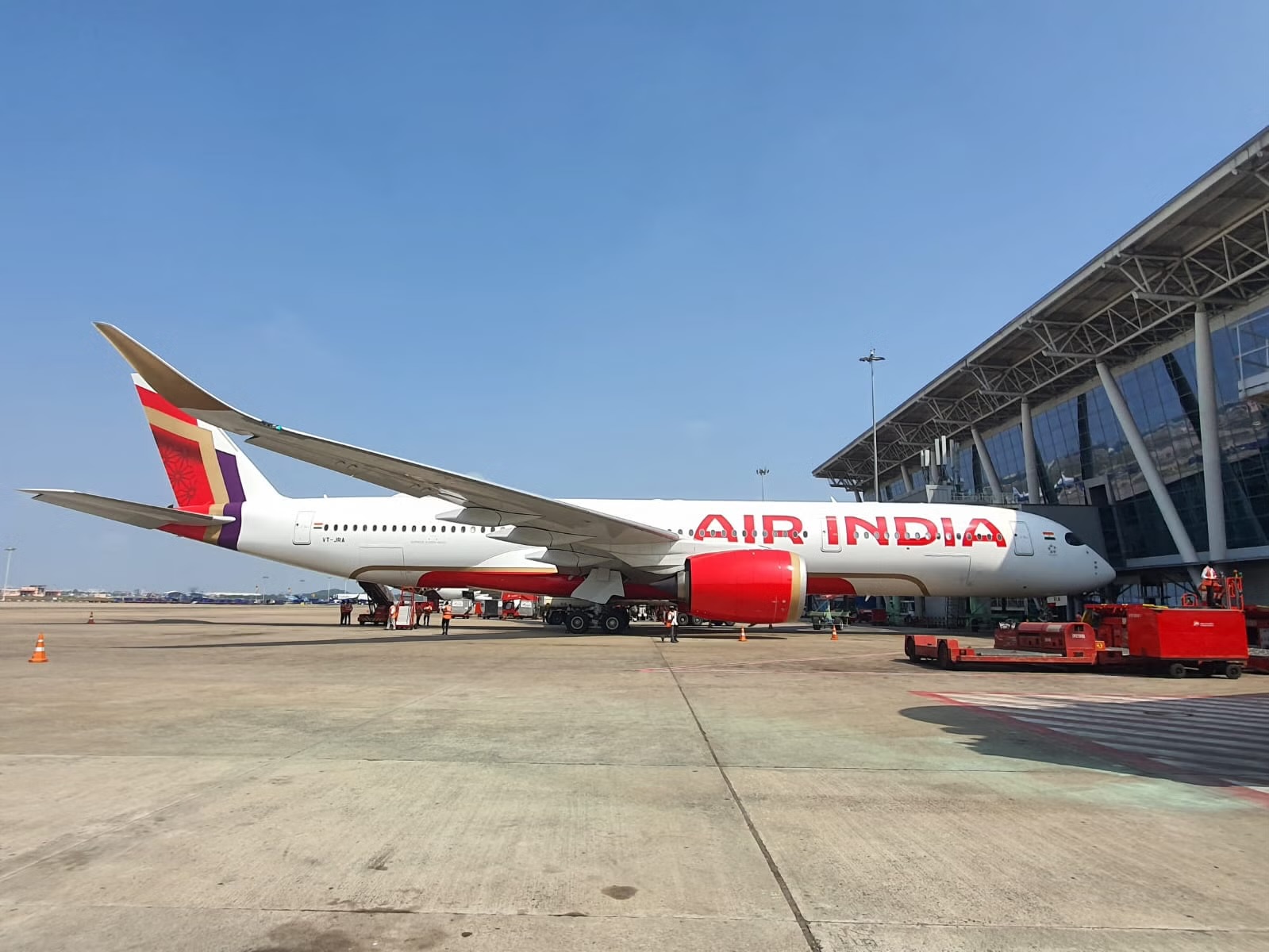 A red and white Air India jet parked in front of an airport terminal building.