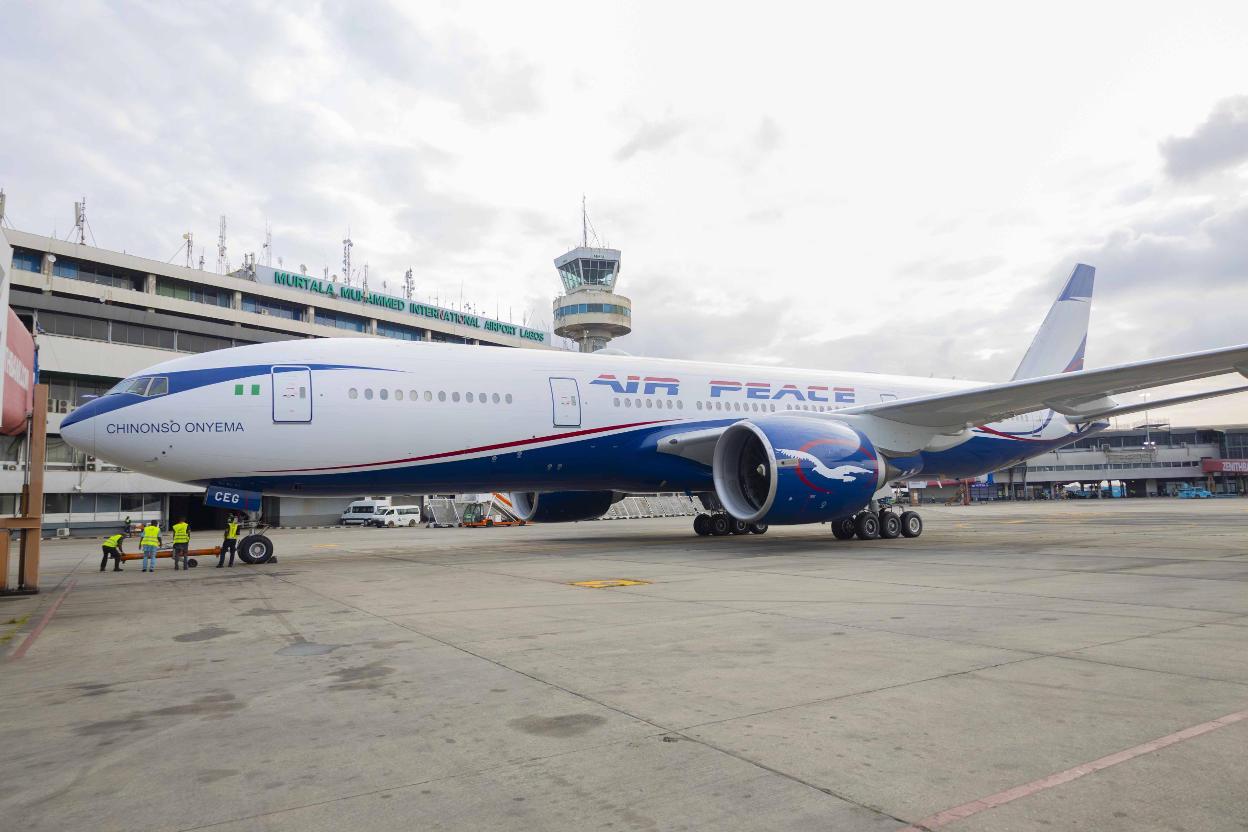 A blue and white Air Peace jet parked outside LOS airport in front of a cloudy sky.