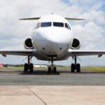 A head-on shot of an Alliance Airlines Embraer E190 sat on a runway in front of a grassy verge and a cloudy sky.