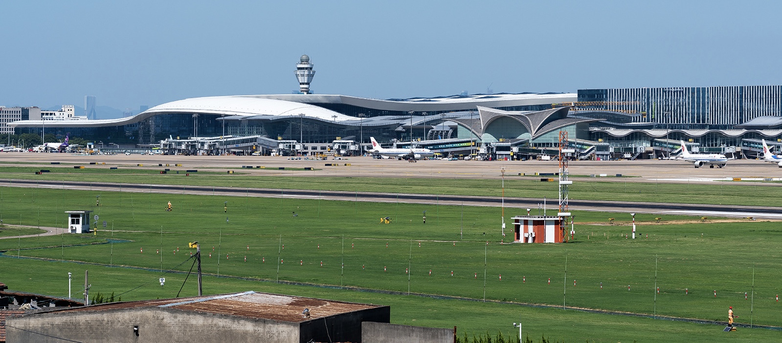 Hangzhou Xiaoshan International Airport (HGH) on a clear day. The Airport terminal is visible behind a runway and a grassy field.