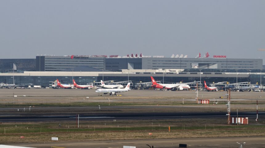 Red and white planes sat on a runway in front of Shanghai Hongqiao International Airport (SHA). There is a grey sky behind them.