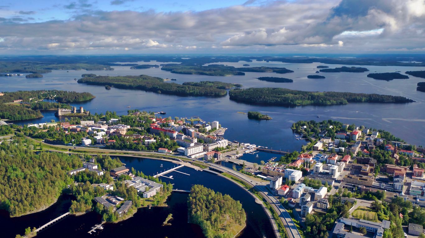 An aerial shot of Savonlinna showing a series of interconnected islands in a deep blue lake, beneath a cloudy sky.