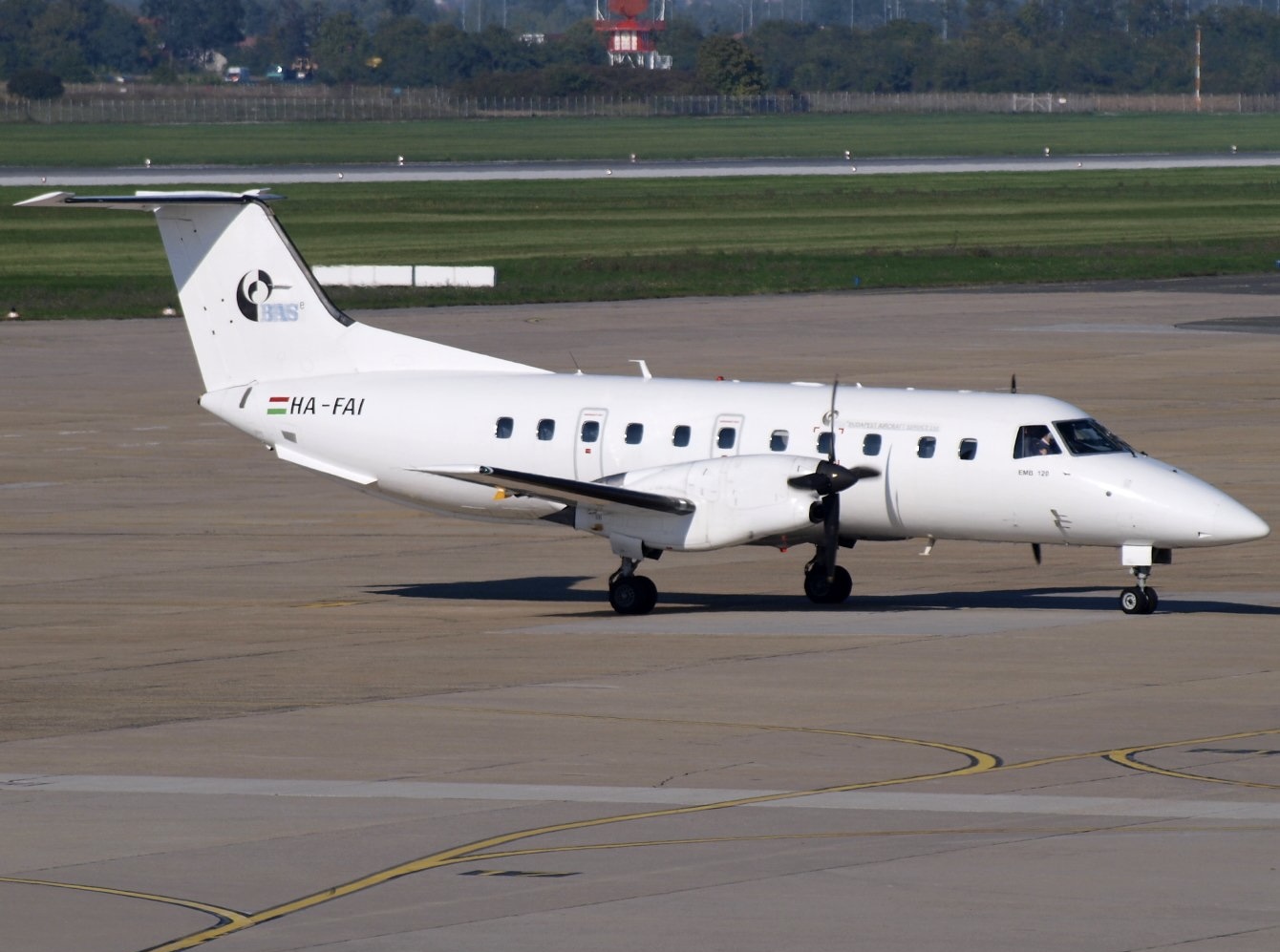 A white Budapest Air Service (BASe) Embraer E120 jet sat on a runway in front of a grassy verge.