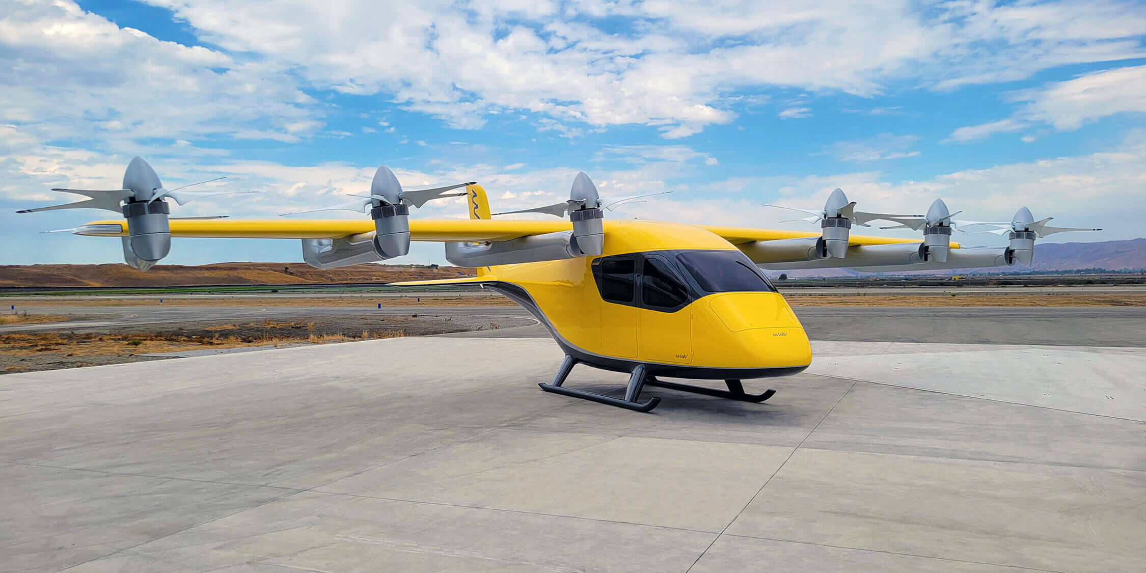 A yellow Wisk Aero aircraft sat on a grey landing strip. A cloudy blue sky is visible behind the aircraft.