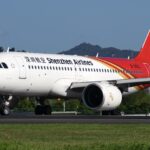 A white, red, and yellow Shenzhen Airlines jet sat on a runway, behind a dark green field.