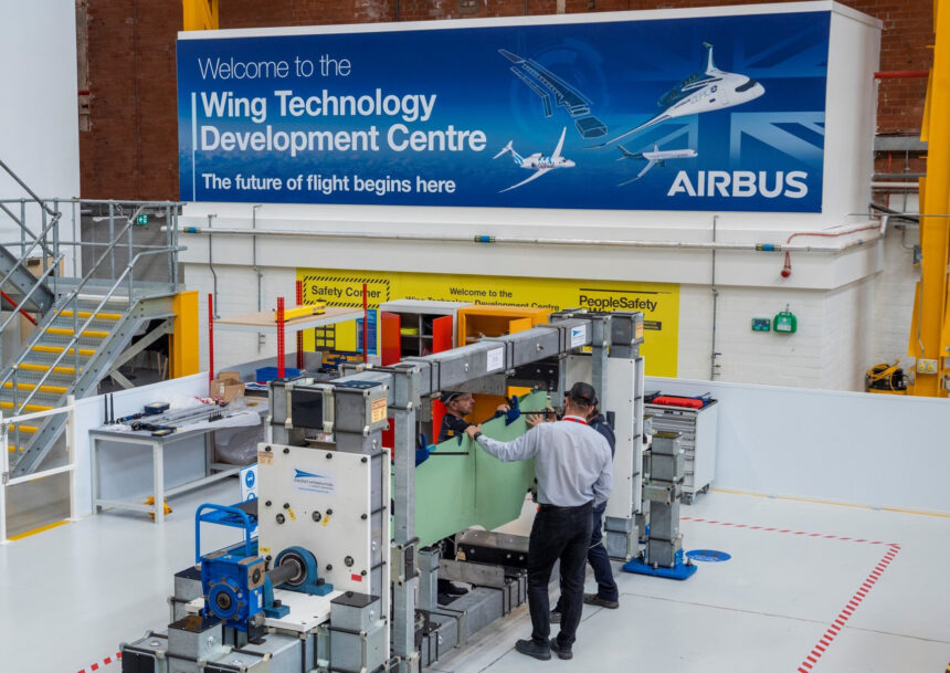 Airbus employees at the Wing Technology Development Centre in Filton, UK. They are seen working on a production line, in front of a blue sign.