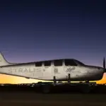 A silver Stralis aircraft at sunset. A line of orange lights illuminates the plane beneath a dark blue sky.